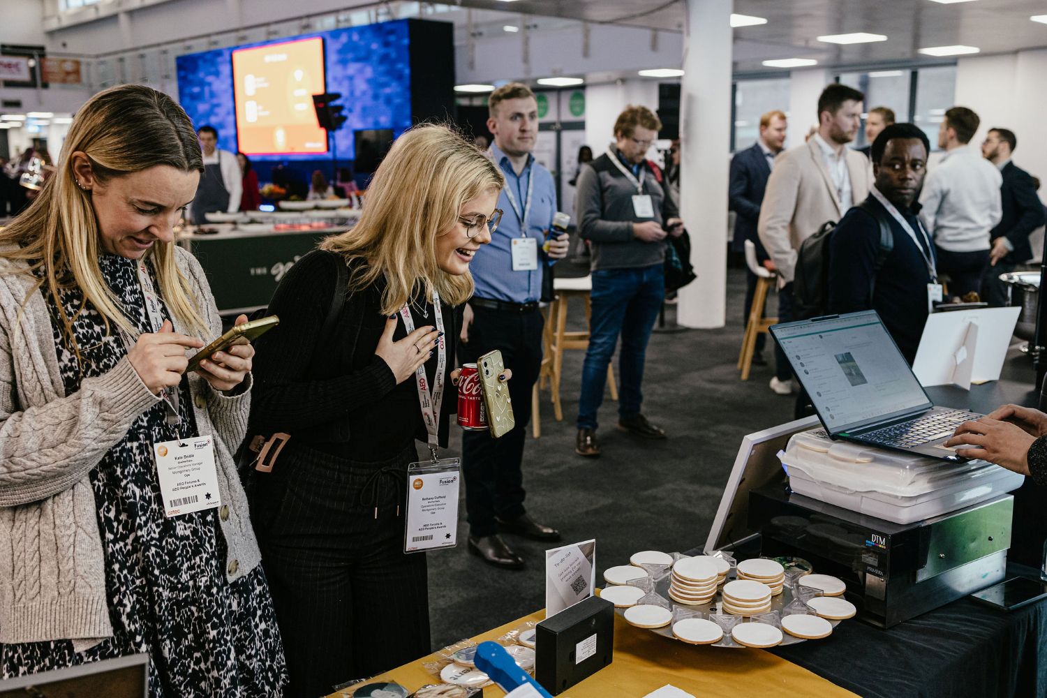 Visitor watching live biscuit printing at an event, as a team member from The Biskery demonstrates the on-site branded biscuit printing service to showcase the impact this for businesses to engage with their clients.