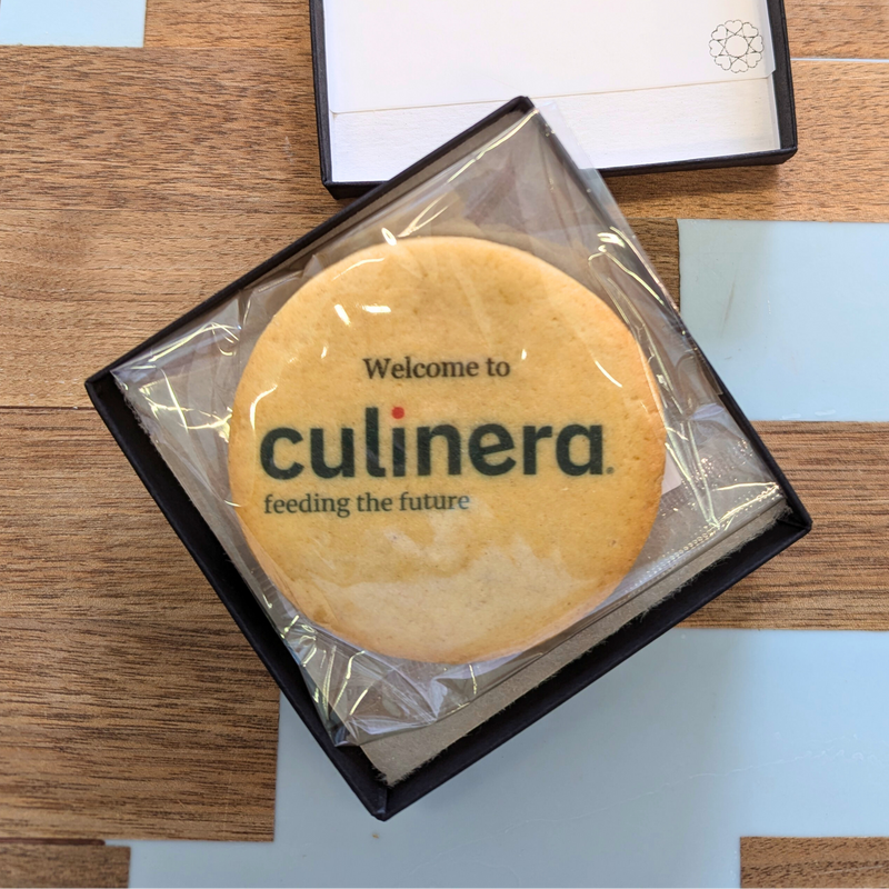 A branded cookie with the "Culinera" logo and tagline rests in a small black gift box with a welcome message.