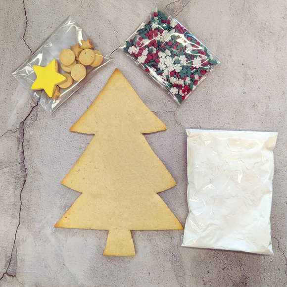A Christmas tree biscuit kit, a bag of sprinkles, and a bag of icing sugar on a table.