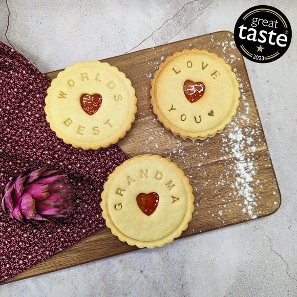 Wooden cutting board with three biscuits, two with the words 'LOVE you' and 'WORLDS BEST' and one with the 'Grandma'