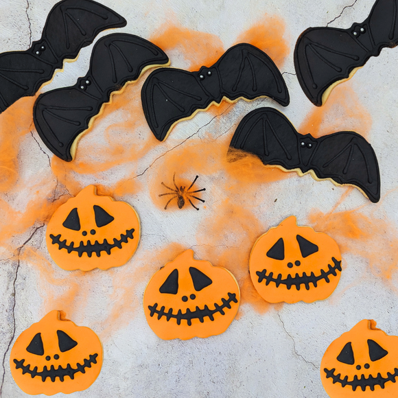 a group of Halloween biscuits in the shape of pumpkins and bats, decorated with black and orange icing.