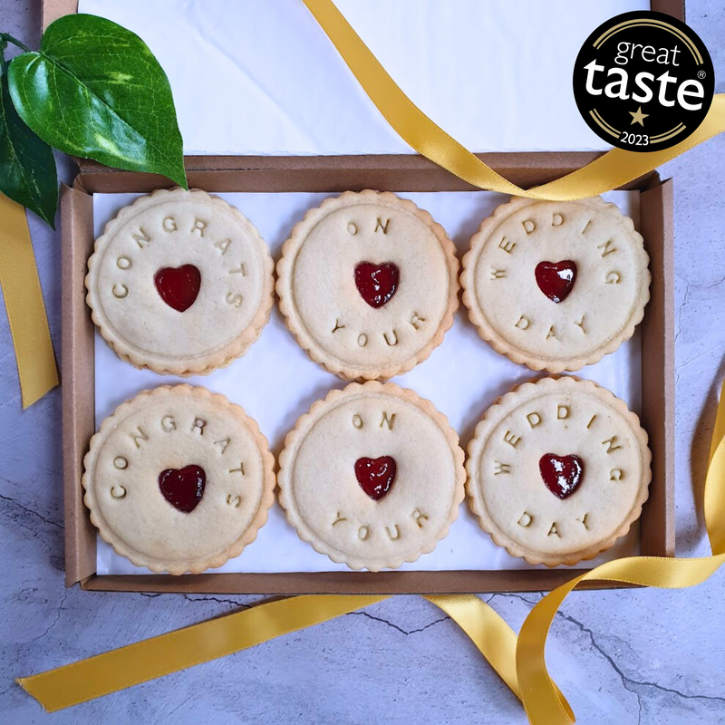 A box of six bespoke jam biscuits with heart-shaped cut-outs in the middle. The biscuits are decorated with the words 'Congratulations on your wedding!'