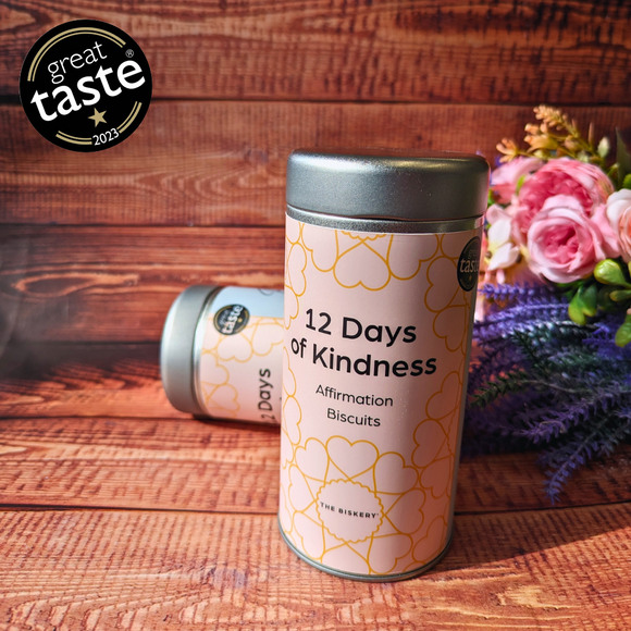 A can of biscuits labeled "12 Days of Kindness." The can is sitting on a wooden table
