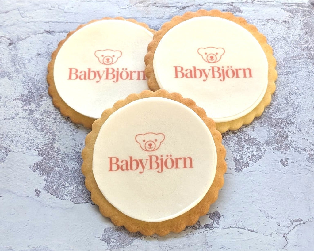 Three round scalloped-edge cookies with white icing, each printed with the red text 'BabyBjörn' and a small teddy bear logo, arranged on a textured light gray surface.