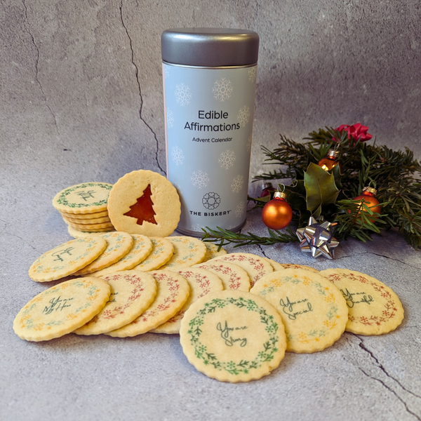  tin of Edible Affirmations next to a stack of Christmas cookies