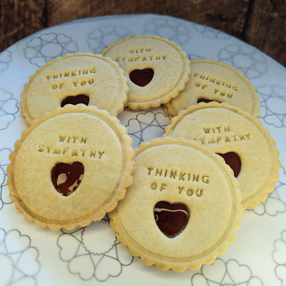 Plate of jam biscuits from The Biskery company, adorned with words 'THINKING OF YOU' and 'WITH SYMPATHY', featuring heart-shaped cut-outs