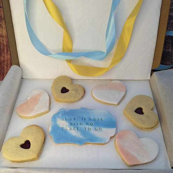 A box with 6 heart-shaped jam and marbled fondant icing biscuits. 1 larger biscuit reads "GRIFF IS LOVE WITH NO PLACE TO GO" in icing.