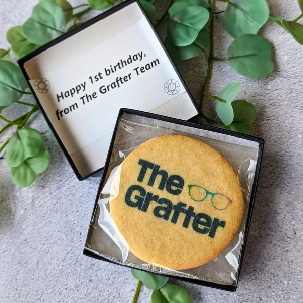 A round butter biscuit with The Grafter logo, individually wrapped in a small black gift box.