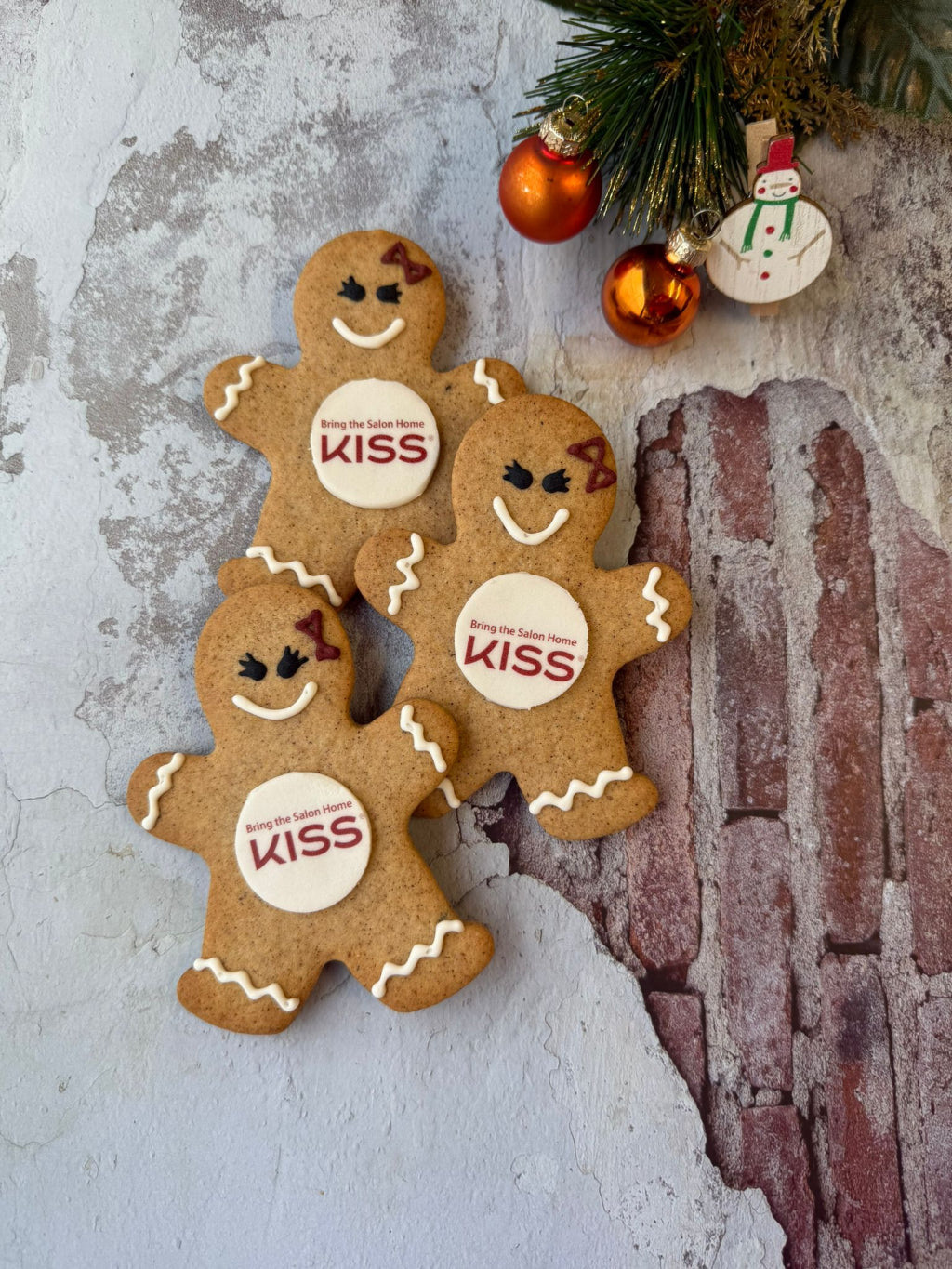 Three hand finished gingerbread men with branded with 'KISS' labels on a textured background with Christmas decorations.