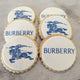 Image of a stack of four cookies with the Burberry logo on them. The cookies are on a white background. The logo is in the center of the cookies and is made up of the words "BURBERRY" in blue letters.