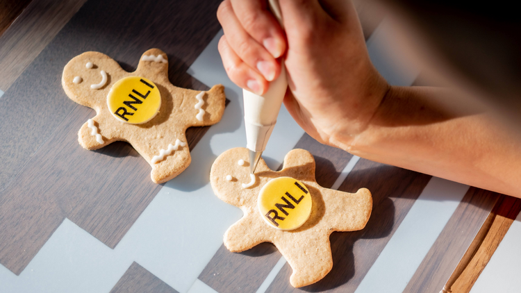 Hand is icing a finishing smile on branded gingerbread man. Perfect for Christmas gifting.