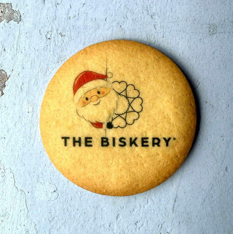 Bespoke Biscuit with a Santa Claus design and 'The Biskery' logo on a light blue background. Great for sustainable Christmas gifts for businesses.