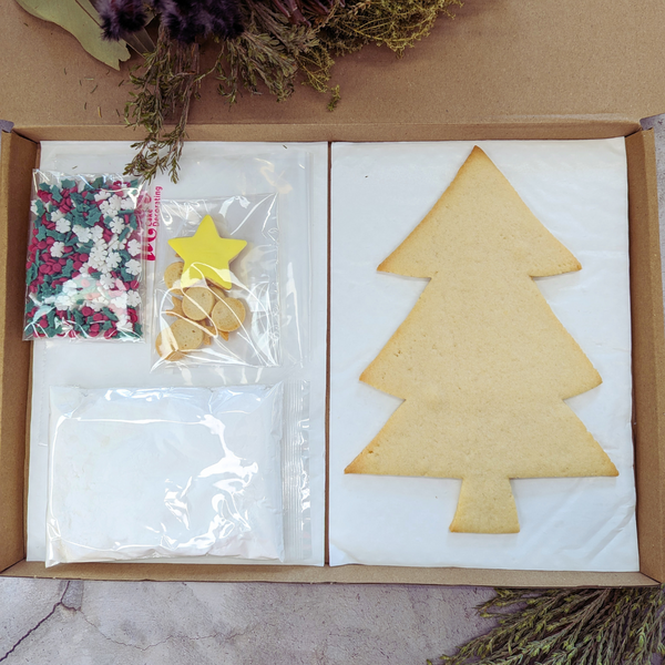 A box from The Biskery containing start kit with a Christmas tree, a bag of sprinkles and icing sugar next to it