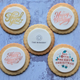 Biscuit with messages 'Thank You', 'Happy Birthday', 'The Biskery', 'Happy Anniversary', and 'Have a Very Merry Christmas' on a textured blue surface.
