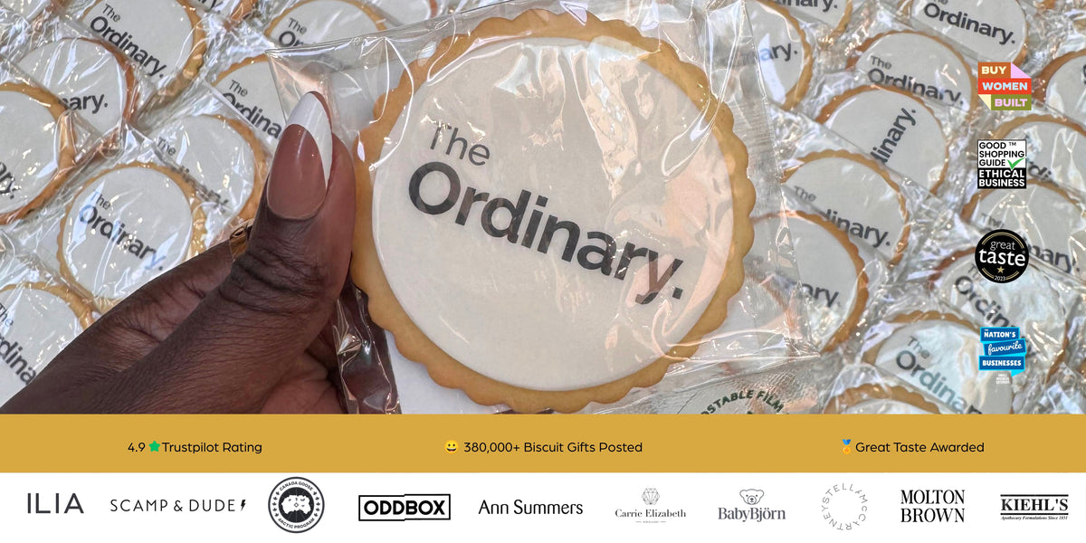 A hand holds a scalloped round biscuit printed with the words 'The Ordinary.' in dark gray text on a warm cream background.
