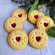Round cookies with red heart centers and engraved text on a light blue surface with green leaves.