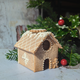 Small gingerbread house decorated with white icing and gingerbread men, placed on a table beside a pile of biscuits