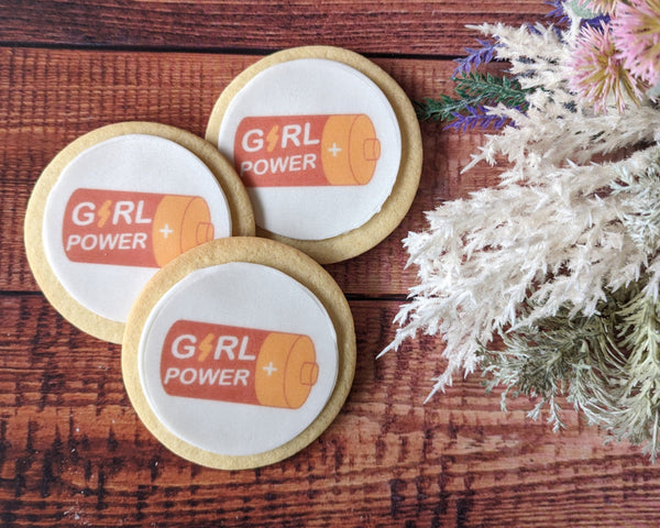 Three cookies with 'Girl Power' design on a wooden surface with decorative elements.