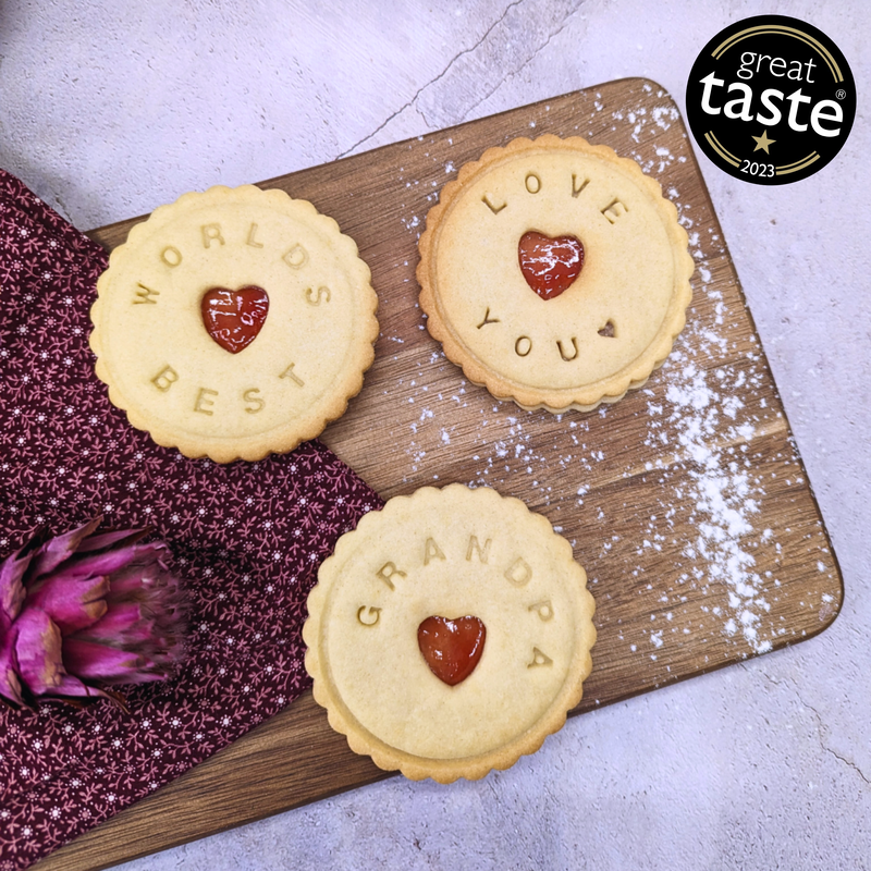 Three cookies with messages on a wooden board, featuring a 'Great Taste' award badge.