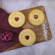 Three jam biscuits with messages 'Worlds Best', 'Love You', and 'Grandma' on a wooden board. Handmade in The Biskery.
