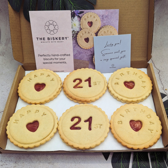 Box of Happy 21st Birthday biscuits with a white ribbon and heart-shaped cookies inside.