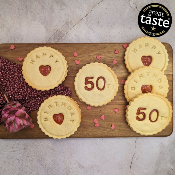 A wooden cutting board topped with delicious-looking biscuits, one of which is decorated with the words 'Happy 50th Birthday'