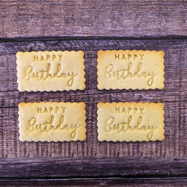 Four rectangular cookies with 'Happy Birthday' embossed on them, placed on a wooden surface.