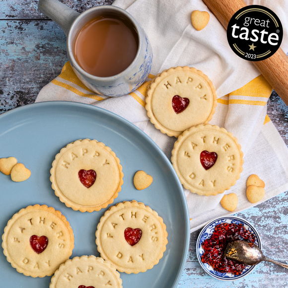 A festive still life with Jam Biscuits, a heart-shaped cookie, and a cup of tea, decorated with the words "Happy Father's Day