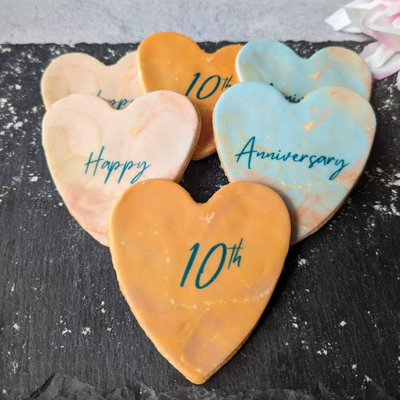 Six heart-shaped iced biscuits with pink and red frosting, arranged on a display stand.  The message "Happy 10th Anniversary" is printed in icing across the center.