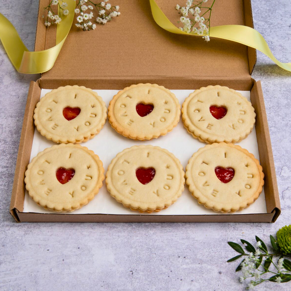 A box of six 'I love you' biscuits with heart-shaped cut-outs and the words 'I love you', accompanied by a flower.