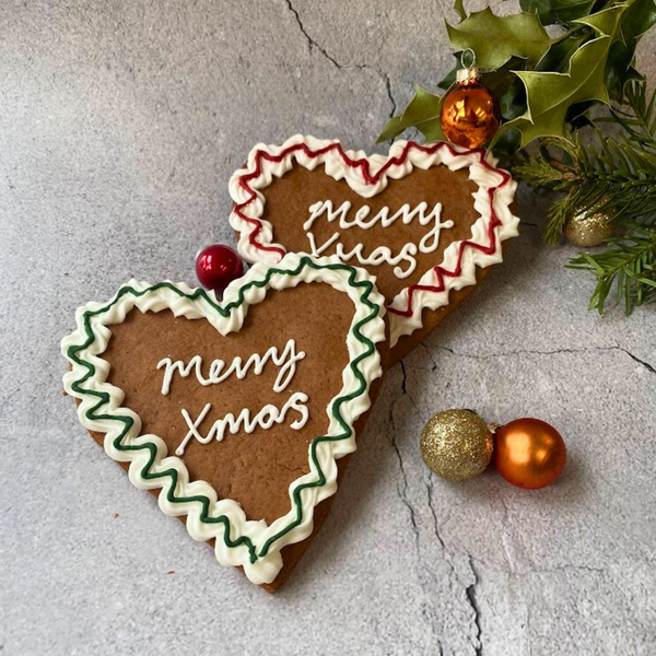 Two iced gingerbread Lebkuchen heart Cookies with "Merry Xmas" message, red & green icing, & festive decorations. 
