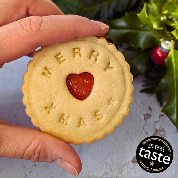 A hand holding an individual Christmas biscuit with a heart in the middle.