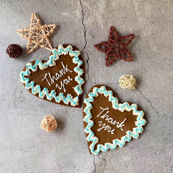 Two iced gingerbread Oktoberfest heart biscuits with the message "Thank you" and decorative icing