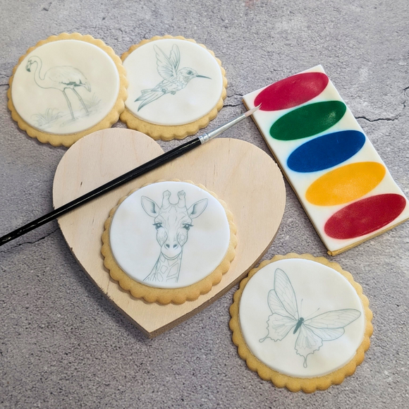 Heart-shaped biscuits with white icing on a tray, with paintbrushes and a colourful palette.