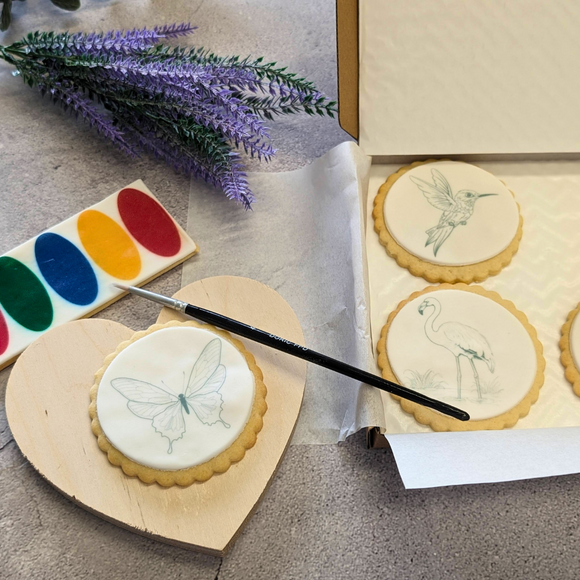 Box of heart-shaped biscuits with white icing and paintbrushes, ready for creative decoration. Paint Your Own Biscuits kit. Fun for all ages!