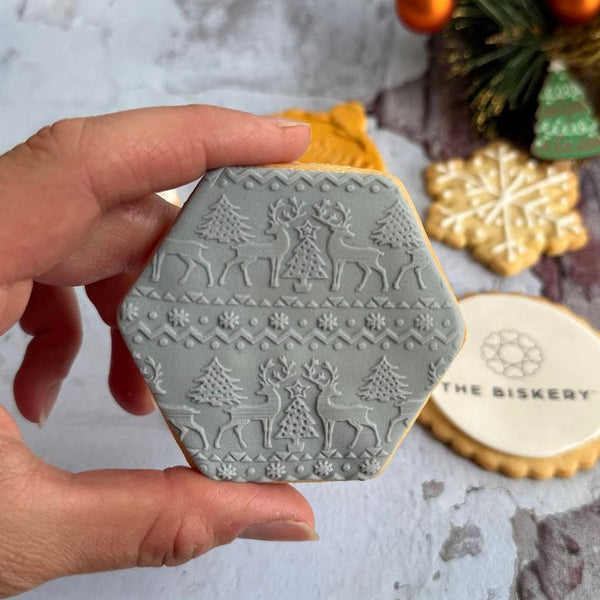 Hexagonal biscuit stamped with embossed Christmas design held by a hand, surrounded by biscuits.
