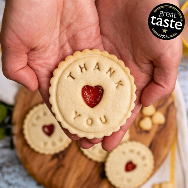 A signature Thank You jam biscuit placed in hands. With more of the same biscuits appearing out of focus in the background.