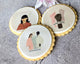 Three printed biscuits with illustrations of people and text on a textured background.