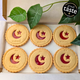 Six round, golden biscuits with red star and crescent jam centres are arranged in a white box. Each is printed with "Eid Mubarak". Green leaves are visible. Star and Crescent Eid Biscuits.