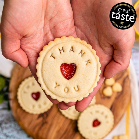 Person holding heart-shaped biscuit with "Thank You" written on it. Biscuit from The Biskery, personalised biscuit company.