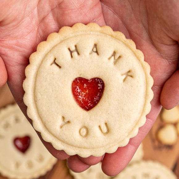 Person holding heart-shaped biscuit with "Thank You" written on it. Biscuit from The Biskery, personalised biscuit company.