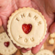Person holding heart-shaped biscuit with "Thank You" written on it. Biscuit from The Biskery, personalised biscuit company.