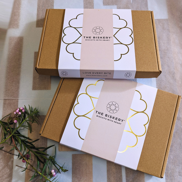 Boxes labelled 'The Biskery' and 'Love Every Bite' sitting on a table, filled with Birthday biscuits.