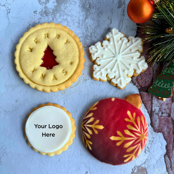 Four cookies with decorative patterns on a textured surface, one with 'The Biscery' branding.

