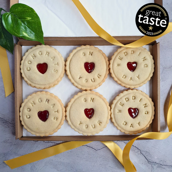 A box of six bespoke jam biscuits with heart-shaped cut-outs in the middle. The biscuits are decorated with the words 'Congratulations on your wedding!'