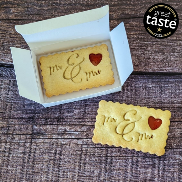 Two butter biscuits with the words "Mr. & Mrs." etched into them, on a wooden table next to a box.