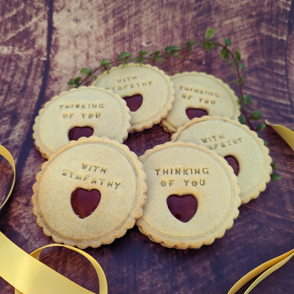 Jam biscuits from The Biskery company on wooden surface, decorated with 'THINKING OF YOU' and 'WITH SYMPATHY', heart-shaped cut-outs