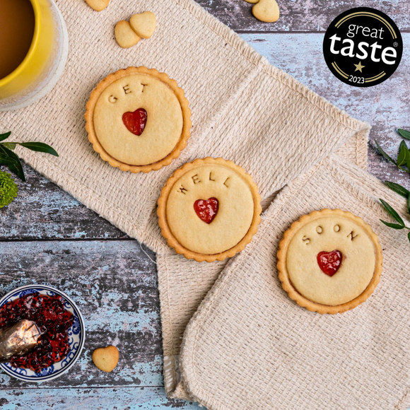 Three heart-shaped biscuits with 'Get well soon' written in jam are on a table