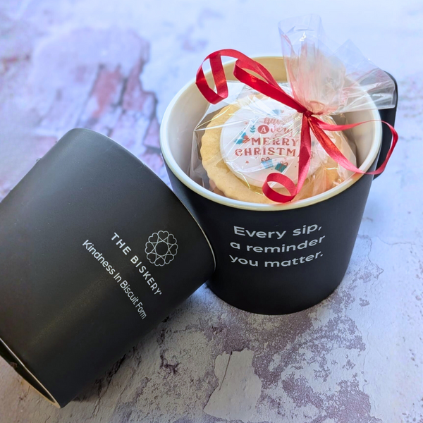 Two black 'The Biskery' mugs; one filled with a Biscuits for a Christmas gift pack, the other showing the side logo.