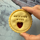No fucks given message biscuit held in hand, round golden cookie with stamped text and heart-shaped jam centre on a textured blue background